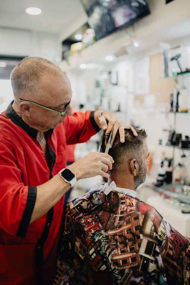 Un barbiere con gli occhiali taglia i capelli a un cliente
